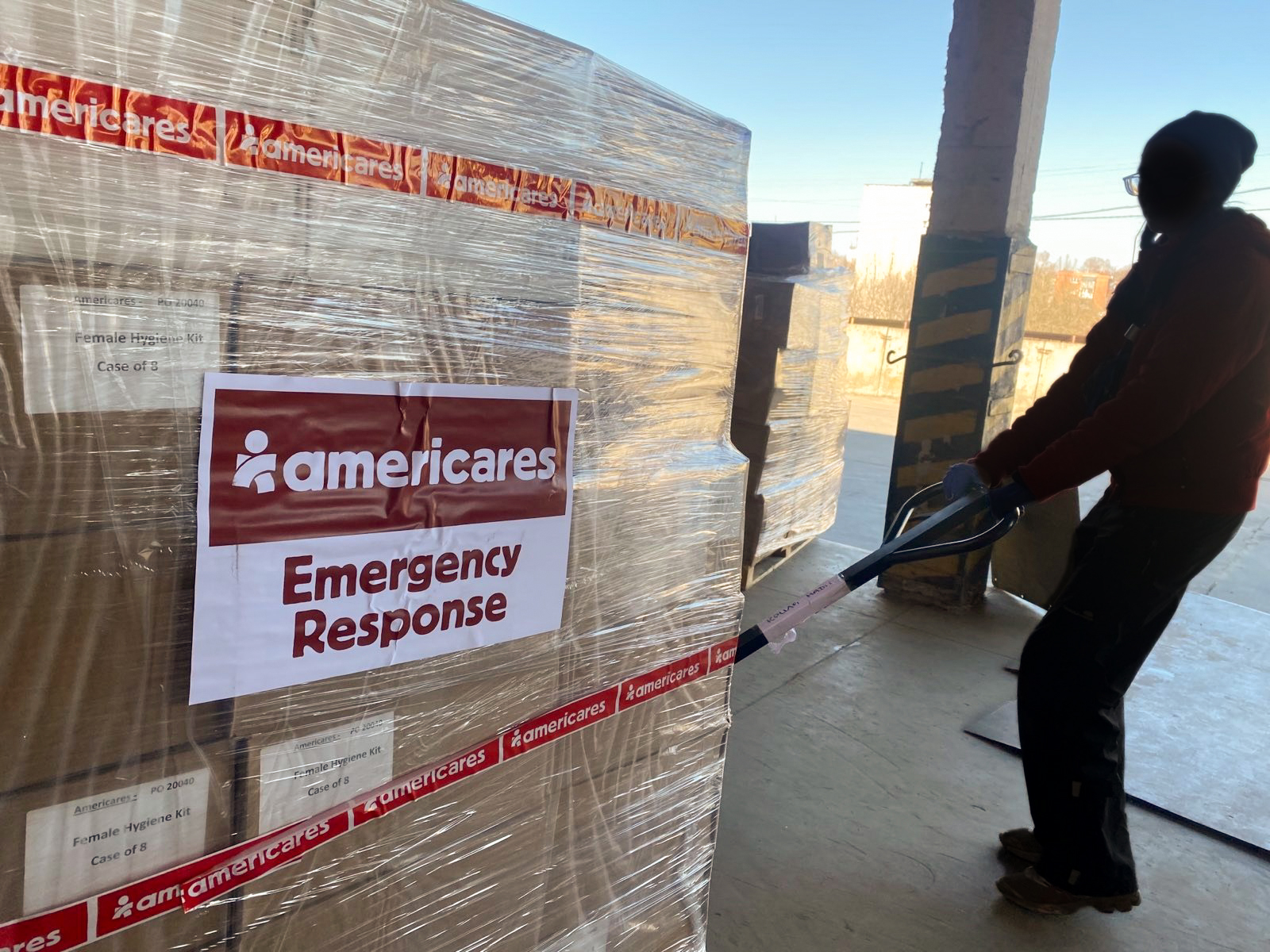 silhouette of worker moving palette of emergency response supplies with americares emergency response branding on the shipment wrapping.