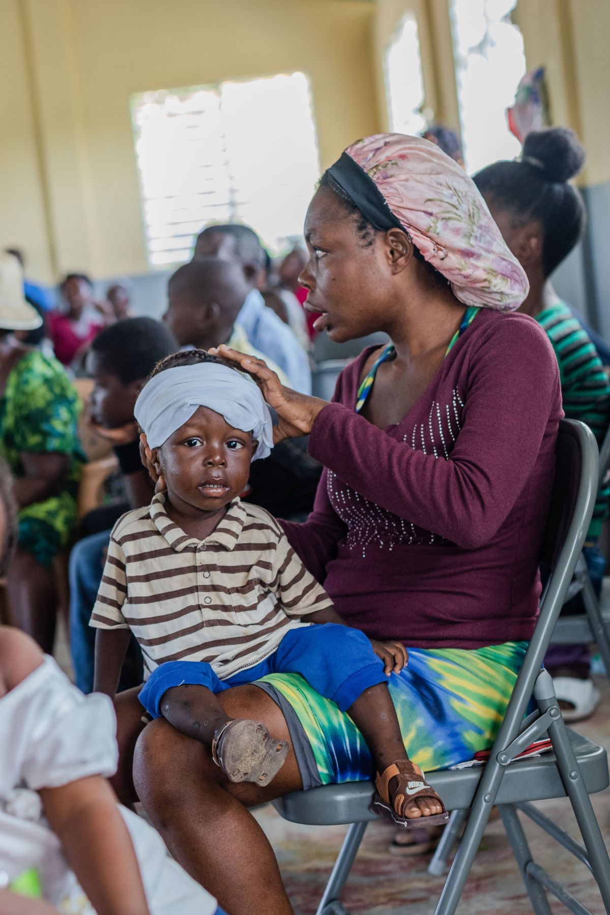 A mother in chair holds her son in lap waiting for health care provider to examine son.