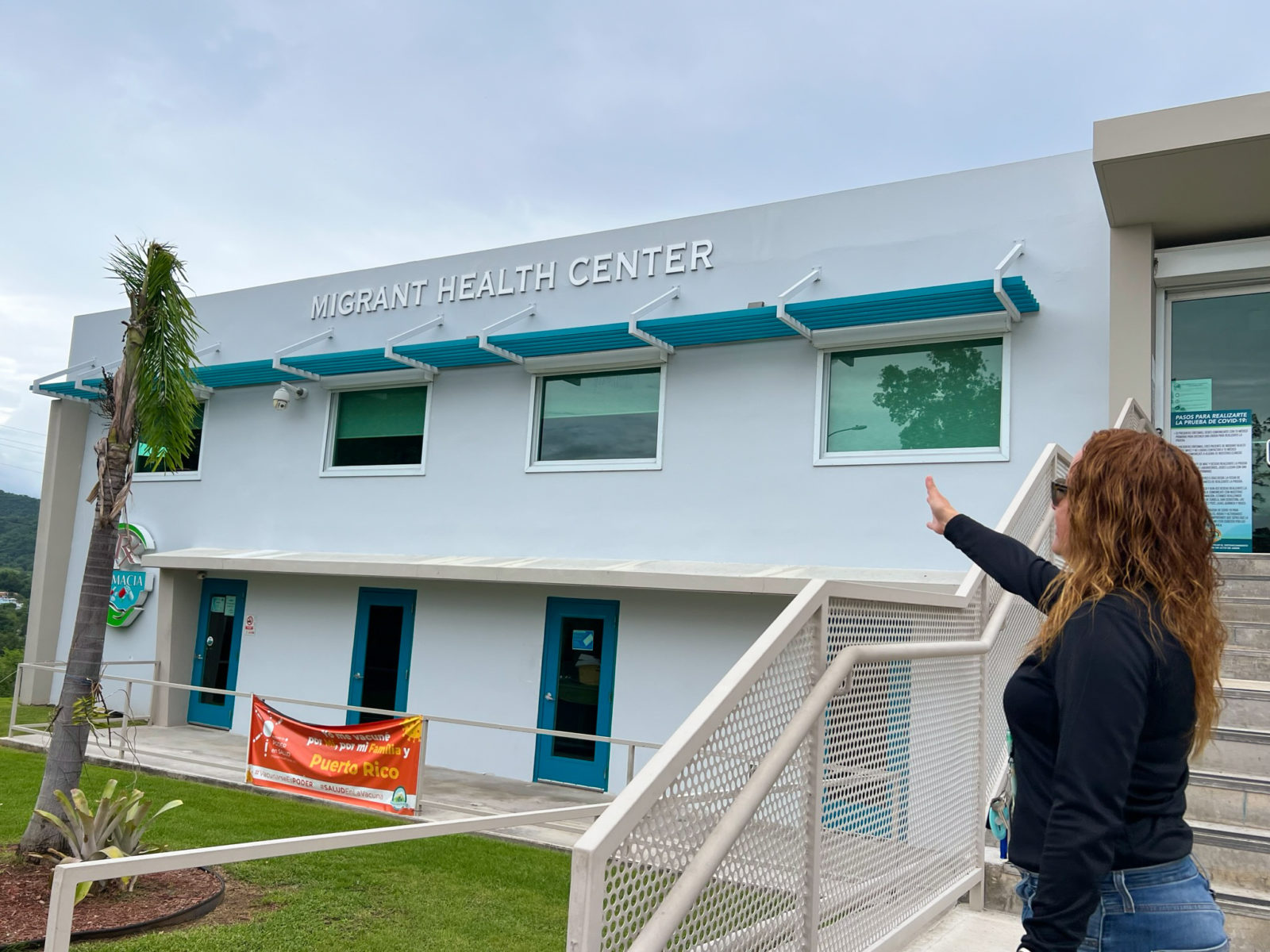 Administrator of the Clinic stands in front of the Migrant Health Center pointing at the solar preparation