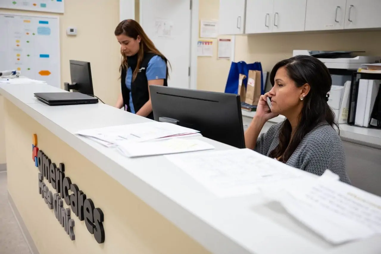 Two women at a reception desk with one holding a phone to her ear.