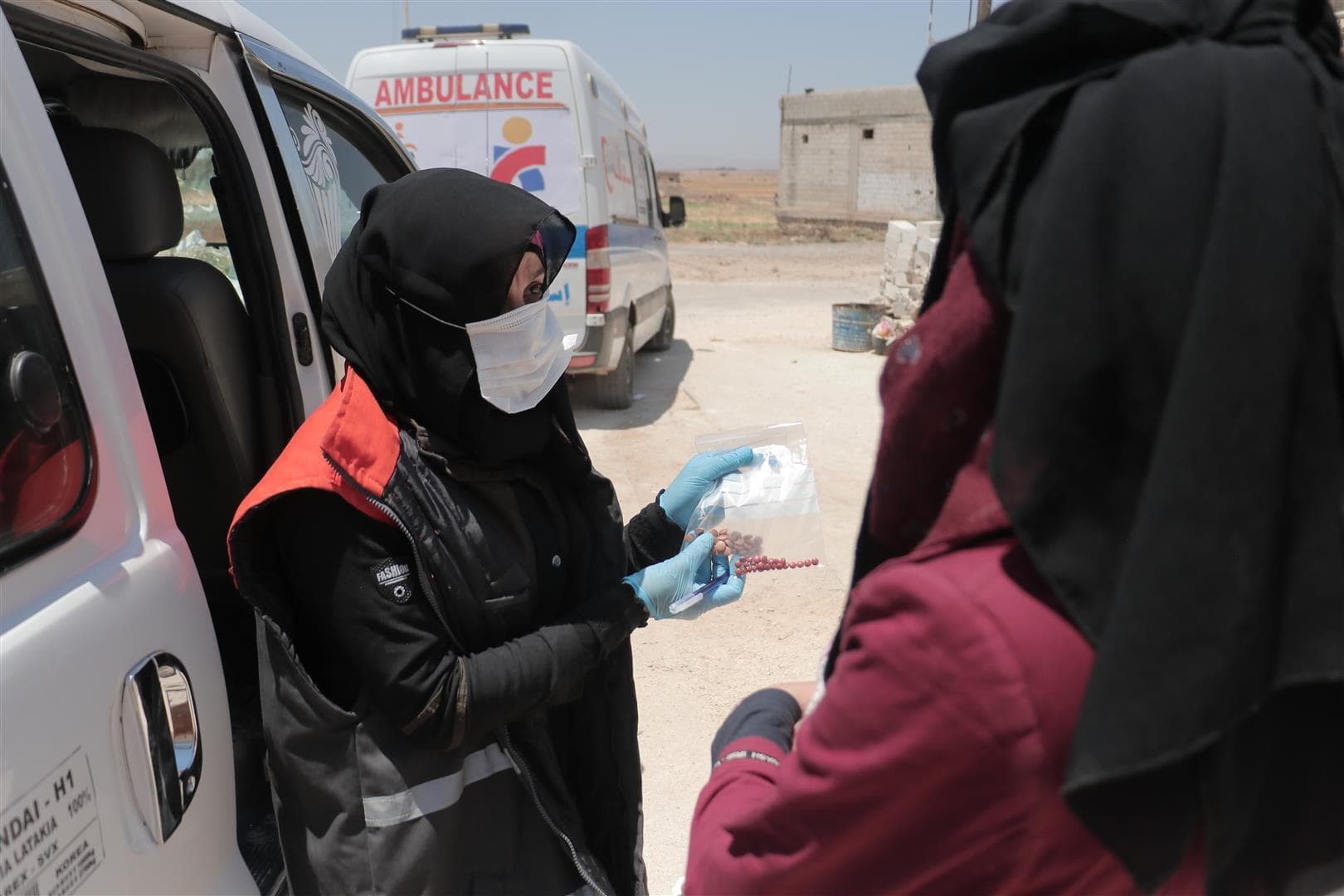 Mobile medical unit on a desert. Two locals discussing medications in front of an open trunk