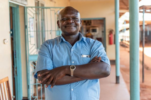 Dr. Matias stands smiling with arms folded in blue shirt in the hospital hallway.