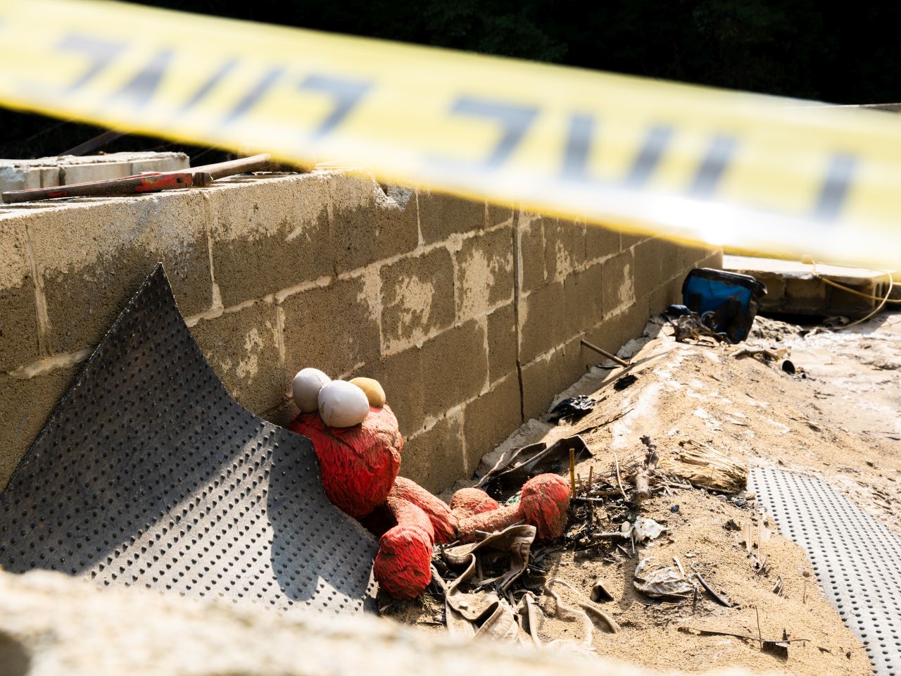 A child's elmo doll sits in rubble beside concrete block wall - all the remains of a house swept away by flood waters.