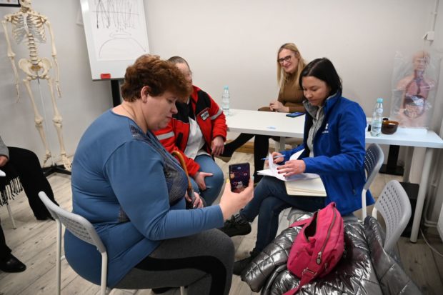 Oksana holds cell phone showing pictures to 3 staff members seated at a table in the clinic.