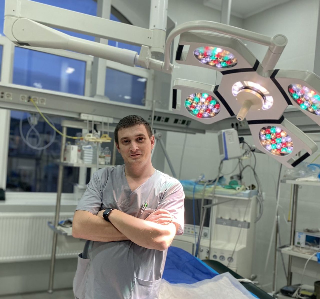 Doctor in operating room in scrubs with view of some of the equipment surrounding him.