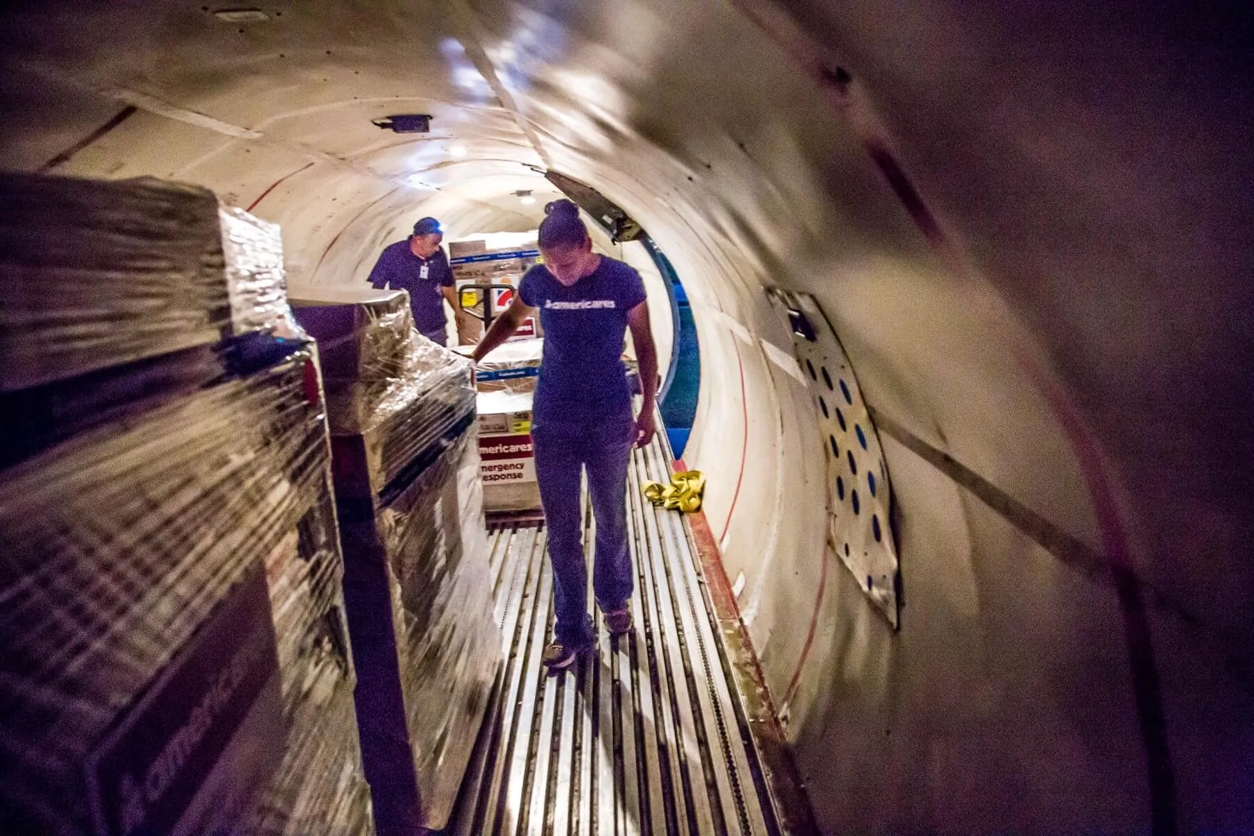 Photo of two Americares workers in the cargo hold of a plane with pallets of supplies.