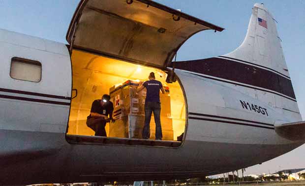 Photo of a cargo hold in a plane open and two Americares staff members readying a pallet of supplies for shipment.