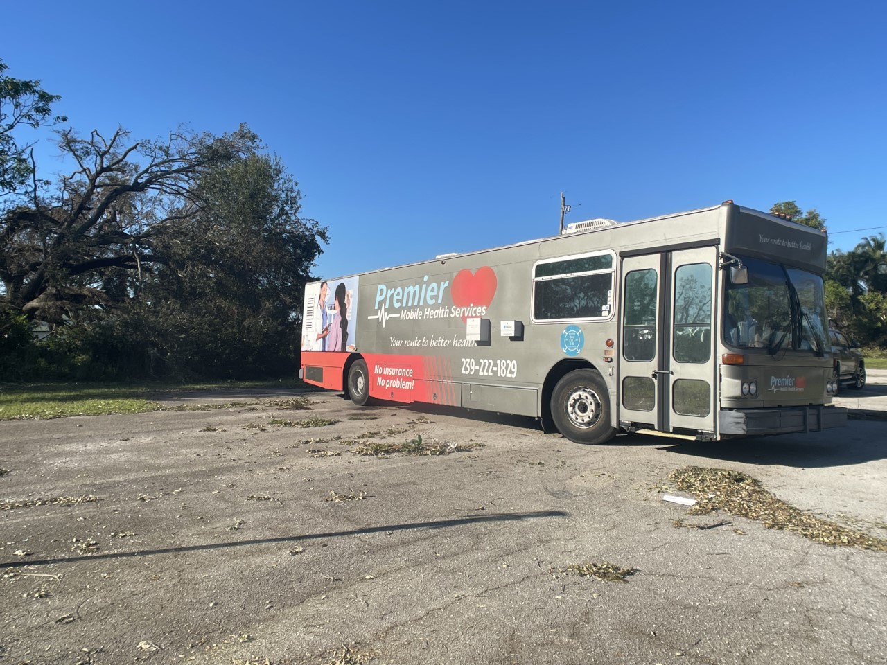 Large grey mobile clinic for Premier Mobile Health Services with phone number, image of patients and "Your route to better health" and "No insurance, no problems" on the side of the vehicle.