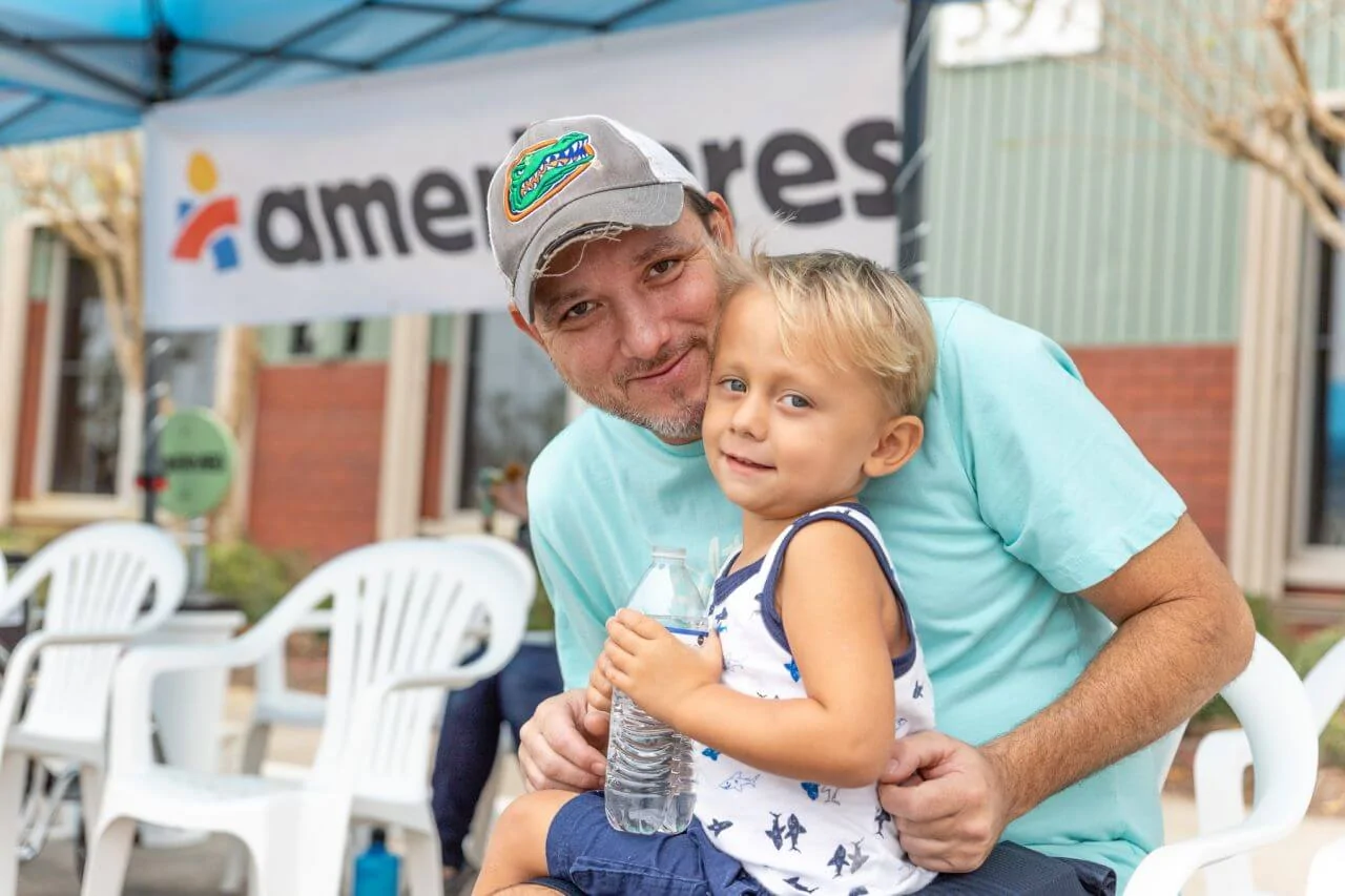 Father and son smile sitting outside an Ameircares clinic.